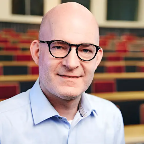'Mann mit Brille in einem Lehrsaal, trägt ein blaues Hemd.