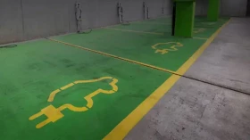 Grüne Parkfläche mit gelben Elektrofahrzeug-Symbolen und Stromsteckern.