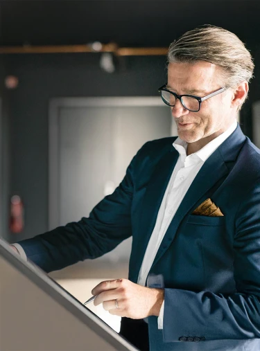Eine Person in einem blauen Anzug hält ein Kunstwerk und schaut es an. Im Hintergrund sind verschwommene Kunstwerke zu sehen.