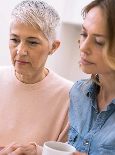 Zwei Frauen schauen konzentriert auf ein Dokument oder einen Bildschirm, eine von ihnen hält eine Brille in der Hand.