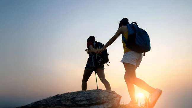 Zwei Personen mit Rucksäcken in einer Berglandschaft bei Sonnenuntergang.