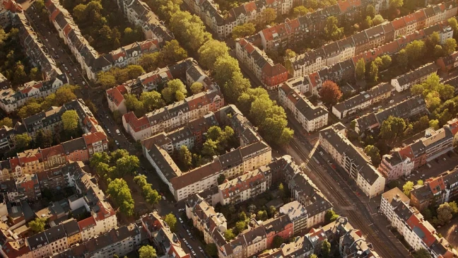 Luftaufnahme eines dicht bebauten Stadtviertels mit Wohnhäusern, begrünten Höfen und baumgesäumten Straßen.
