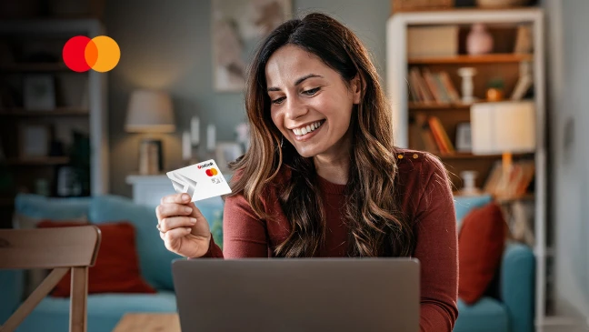 Lächelnde Frau mit Unicreditcard in der Hand sitzt vor einem Laptop