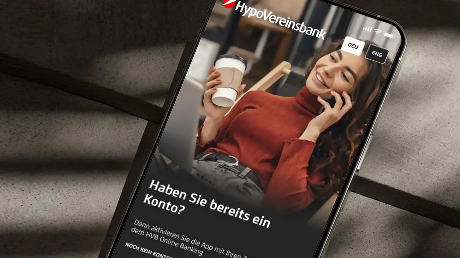 Smartphone mit HypoVereinsbank-App, Frau mit Kaffeetasse und Text zur Kontoaktivierung, darunter zwei Schaltflächen.
