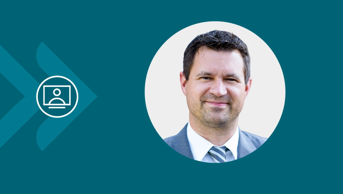 Eine geschäftlich gekleidete Person in kreisförmigem Portrait vor türkisfarbenem Hintergrund mit Video-Symbol.