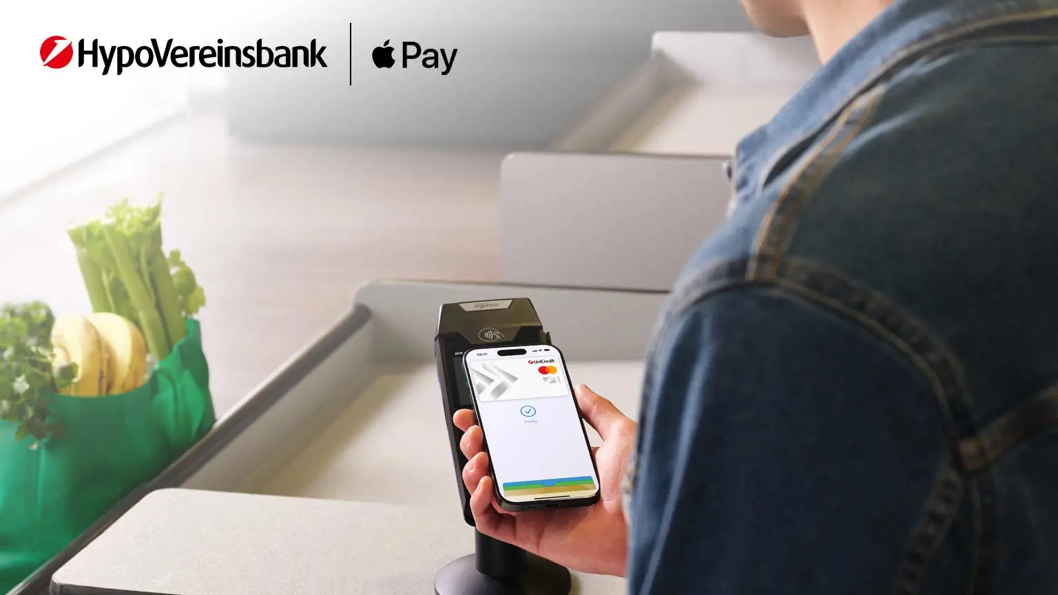 Person hält Smartphone an Kartenlesegerät neben Einkaufstasche, unten Logos von HVB und Apple Pay.