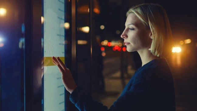 Person in urbaner Umgebung betrachtet ein interaktives Display bei Nacht.