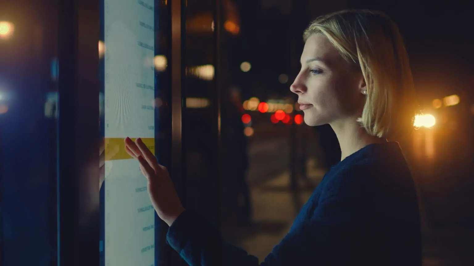 Person in urbaner Umgebung betrachtet ein interaktives Display bei Nacht.