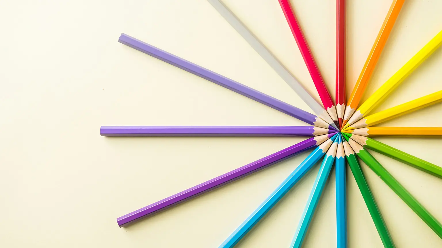Colored pencils in various colors arranged in a circle on a light background, with the tips pointing toward the center.