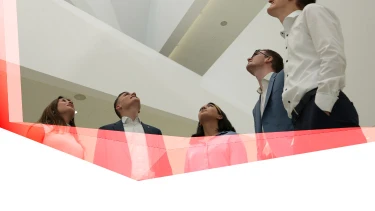 Four people in formal attire standing indoors, viewed from below with ceiling and upper walls visible.
