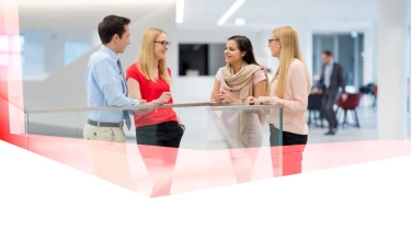 Four people talking in a bright, modern office setting with a blurred background, suggesting a professional meeting.