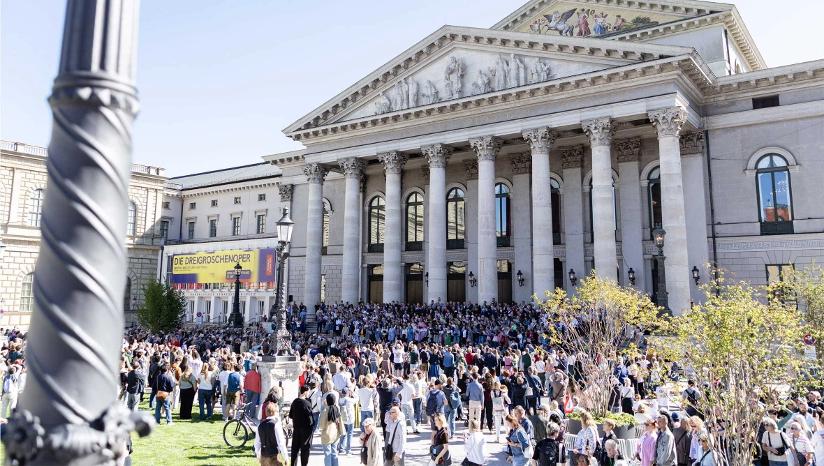 Viele Personen versammeln sich vor einem Gebaeude mit hoher Saeulenfassade und breiter Treppenanlage.