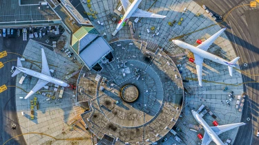 Luftaufnahme eines Flughafenterminals mit drei großen Flugzeugen, die sternförmig am Gate stehen, umgeben von Bodenfahrzeugen und Ausrüstung.