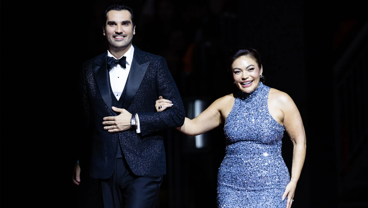 Ein Opernsänger in schwarzem Anzug mit Fliege und eine Opernsängerin in einem grauen Pailettenkleid betreten die Bühne