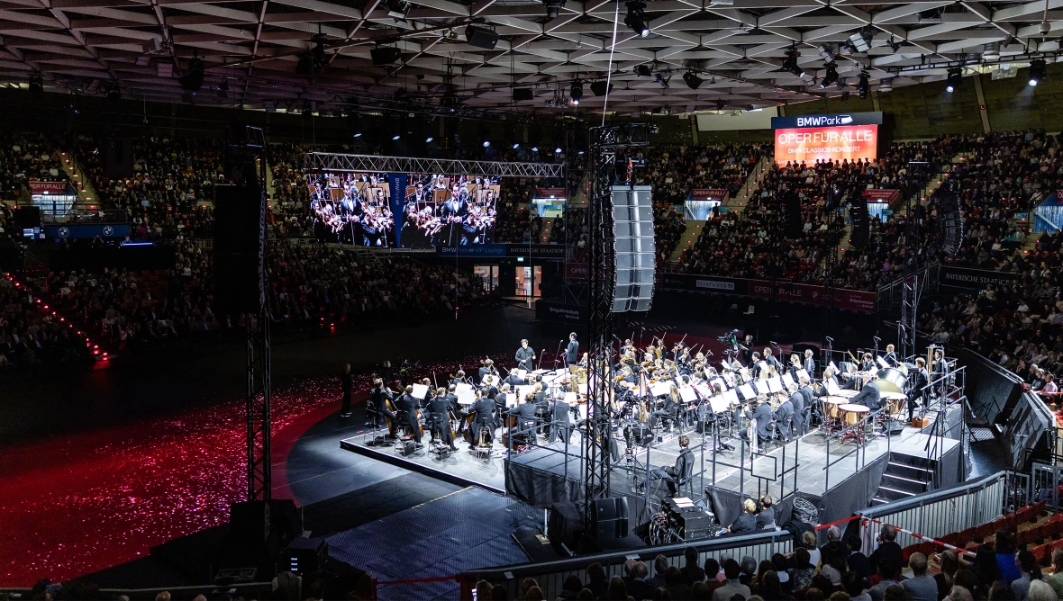 Blick von oben auf die Bühne mit dem Orchester, rundherum voll besetzte Besucherränge