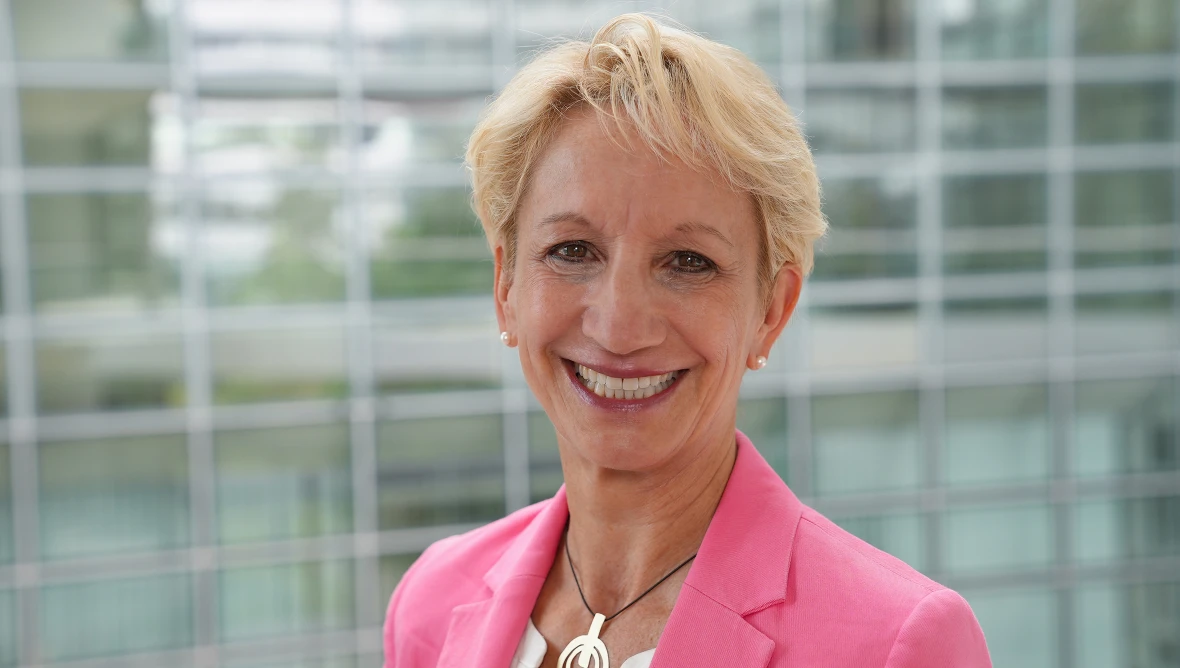Porträt von Birgit Zabel mit kurzen blonden Haaren und pinkem Blazer vor hellem Hintergrund.