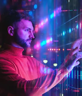 Mann mit Bart und rotem Rollkragenpullover interagiert mit einer virtuellen, farbenfrohen Benutzeroberfläche aus leuchtenden Linien und Punkten in Blau- und Pinktönen.