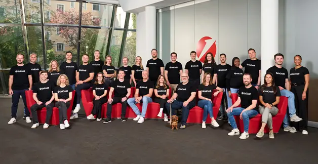 Gruppe von Personen in UniCredit T Shirts im Raum mit rotem Sofa und Hund.