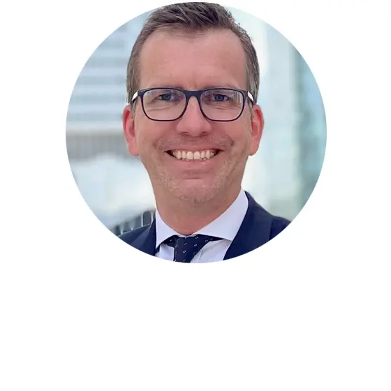 Eine Person in einem formellen Anzug lächelt und schaut in die Kamera. 