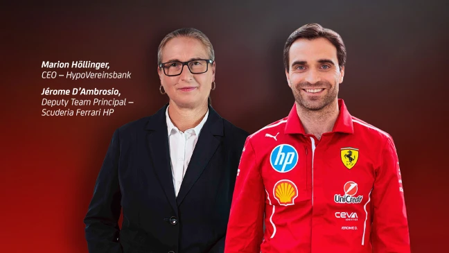 Marion Höllinger, CEO der HypoVereinsbank, steht neben Jérôme D’Ambrosio, Deputy Team Principal von Scuderia Ferrari HP. Beide blicken in die Kamera vor einem Hintergrund mit Farbverlauf von Dunkelrot zu Schwarz. Höllinger trägt einen dunklen Anzug mit weißem Hemd und Brille, D’Ambrosio eine rote Rennjacke mit Sponsorenlogos wie HP, Shell und UniCredit.